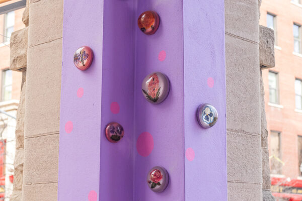 The corner of a lavender wall with embroidery pieces of flowers covered in a dome of resin on it.