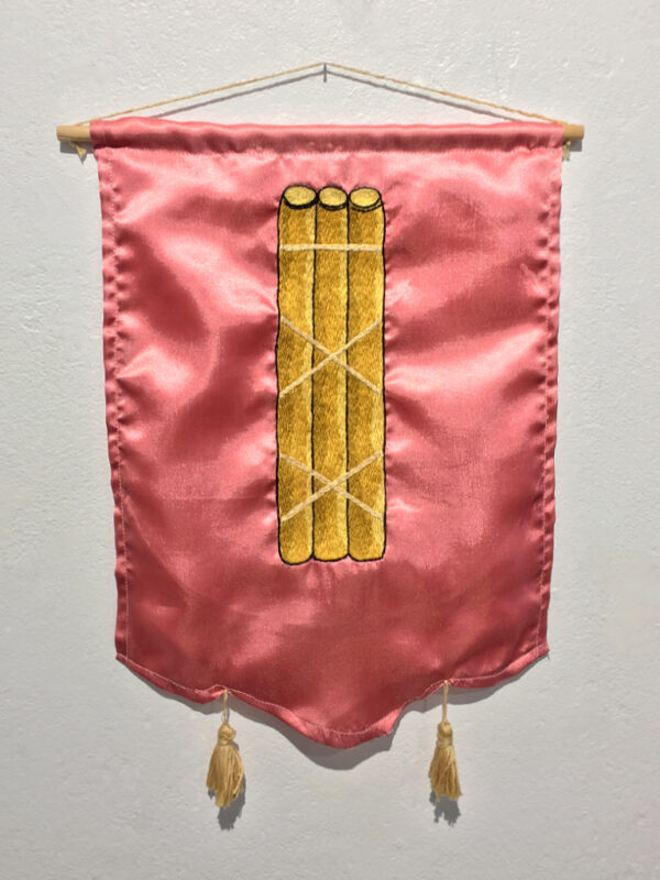 An embroidered tapestry of a bundle of sticks on a pink satin background.
