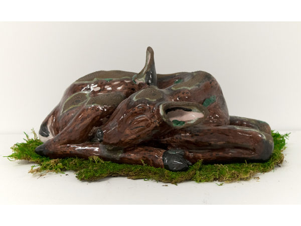A ceramic deer lying on a bed of moss.