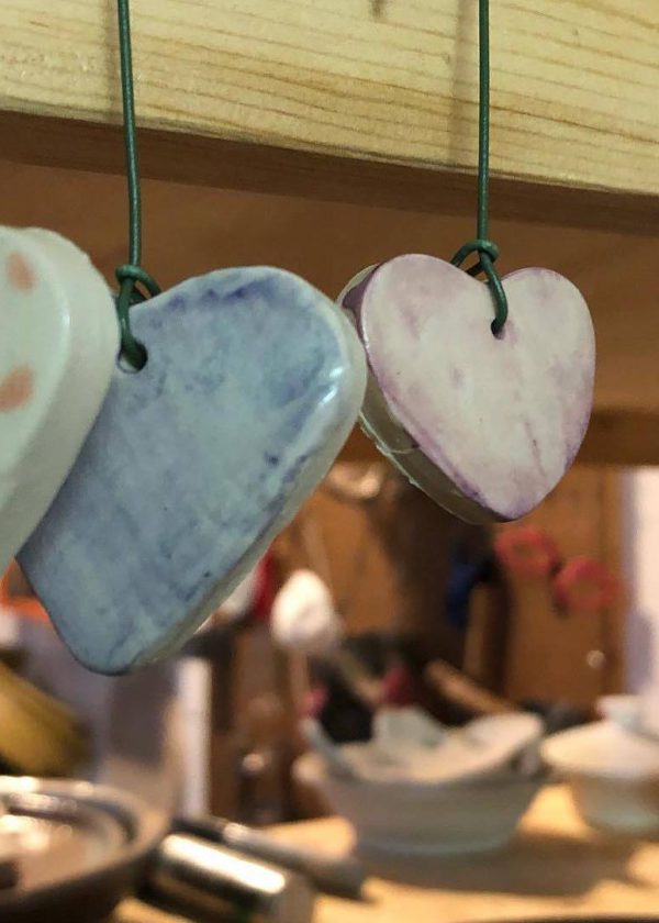 Stoneware hearts in different colours hanging from a wooden display.